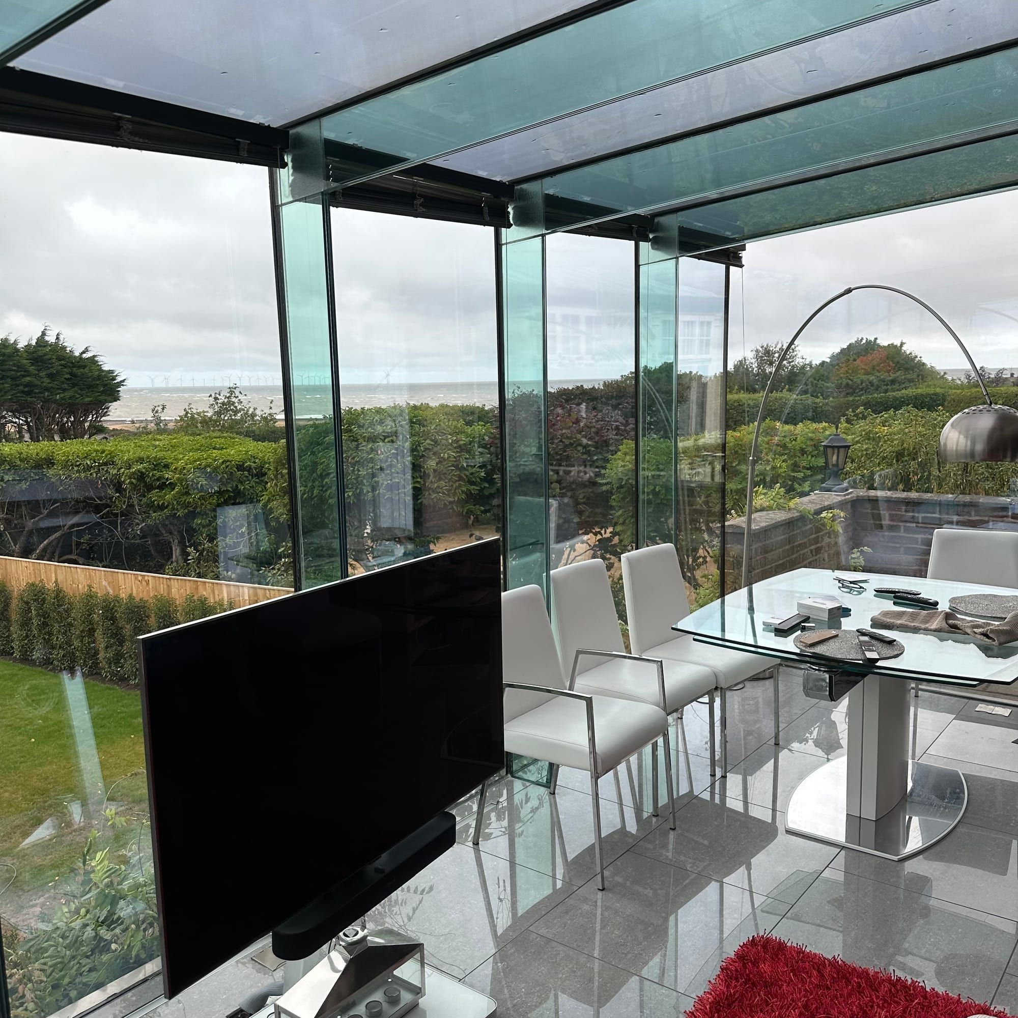 Inside a glass garden room with floor-to-ceiling glazing looking out over a garden towards the sea